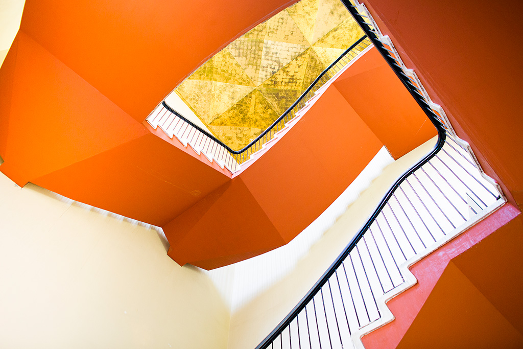 Upward view of a vibrant orange staircase with black handrails and white stairs.